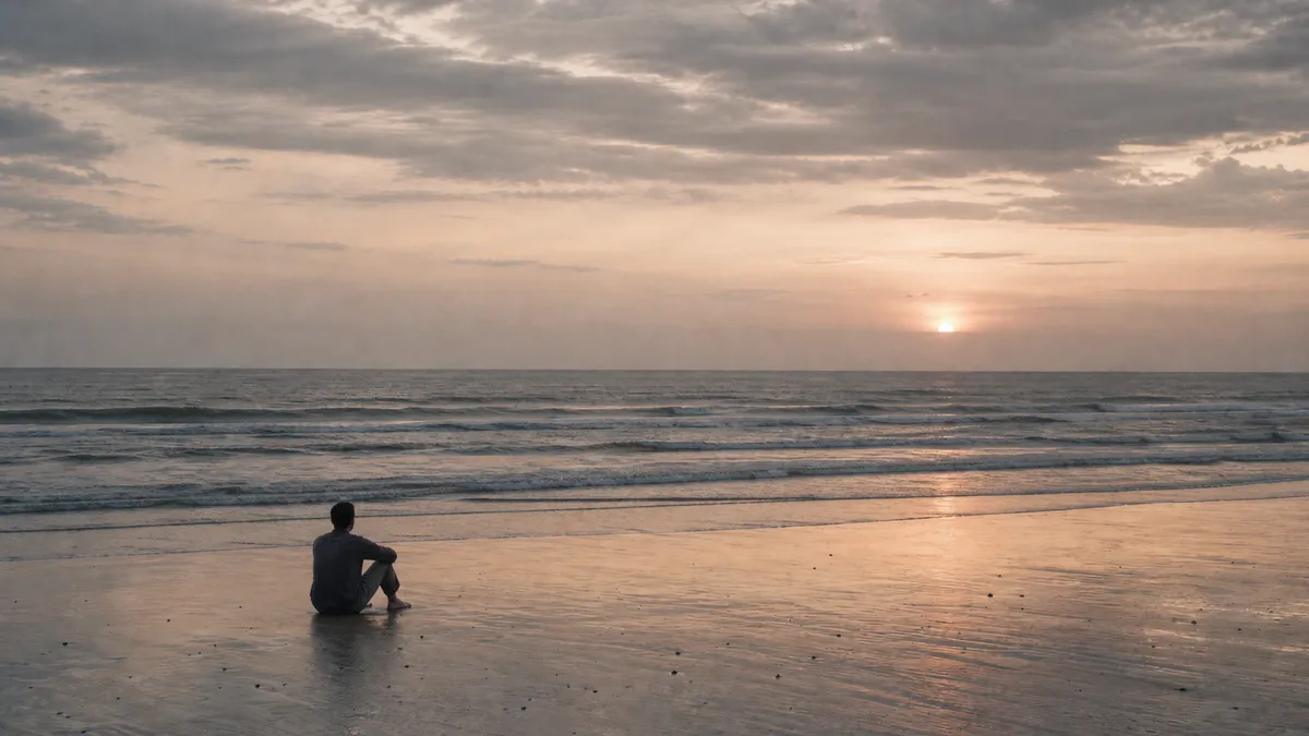 A person sits alone on a wet beach at dusk, knees drawn up, watching the sun sink to the horizon over calm waves.